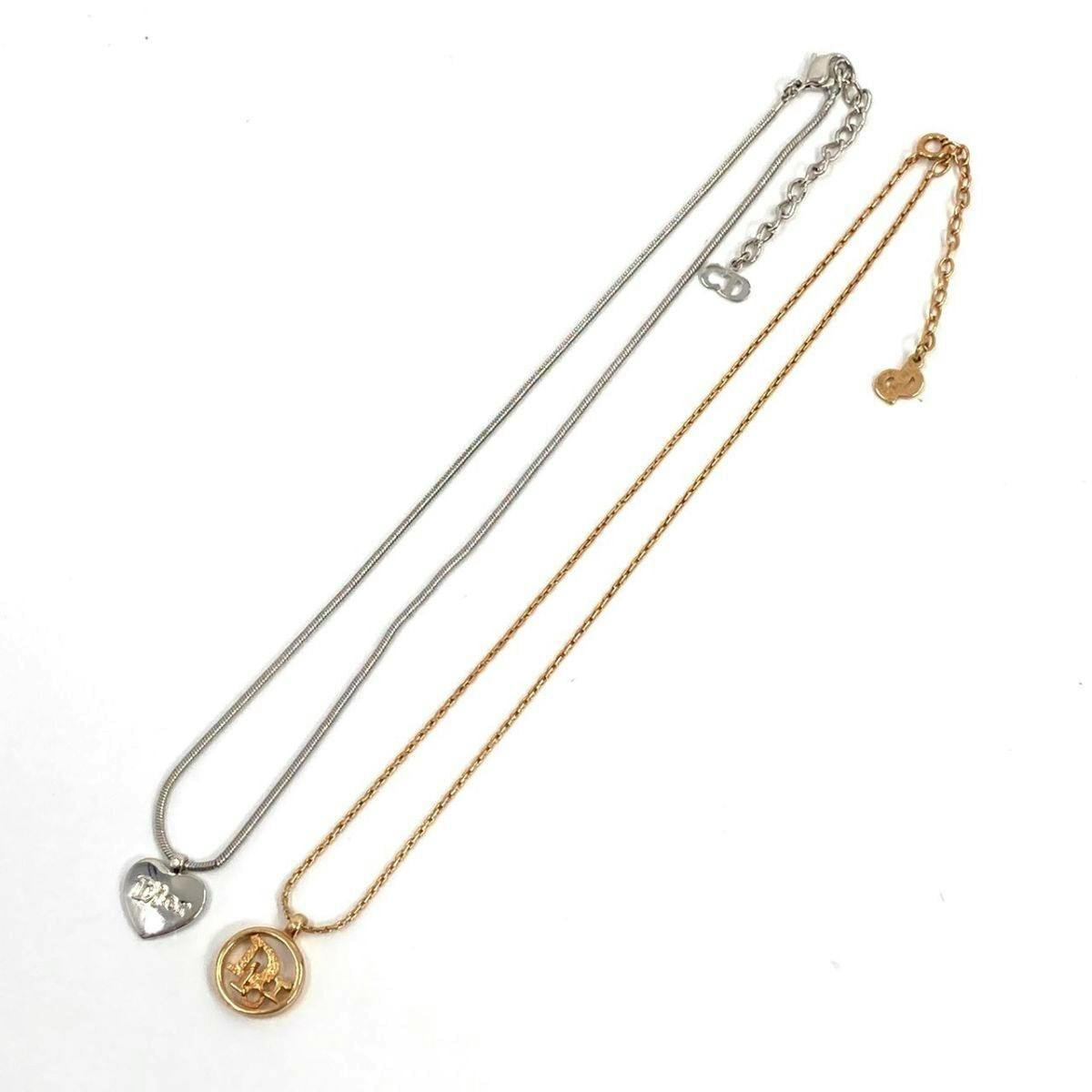 Two Christian Dior necklaces laid flat on a white background: a silver chain with a heart pendant and a gold chain with a round CD-logo pendant.