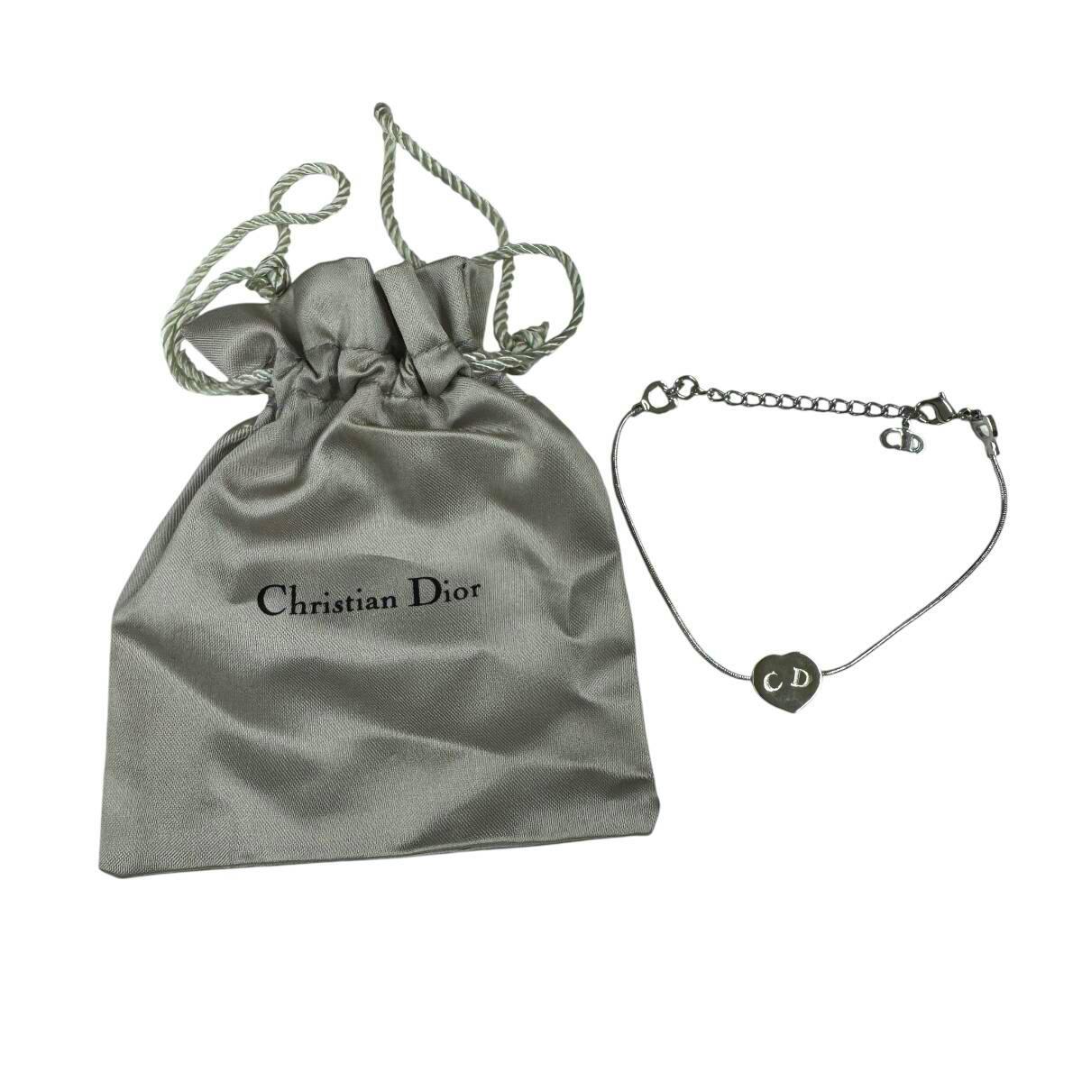 Silver Christian Dior bracelet with a heart-shaped CD charm displayed next to a gray Christian Dior drawstring pouch.