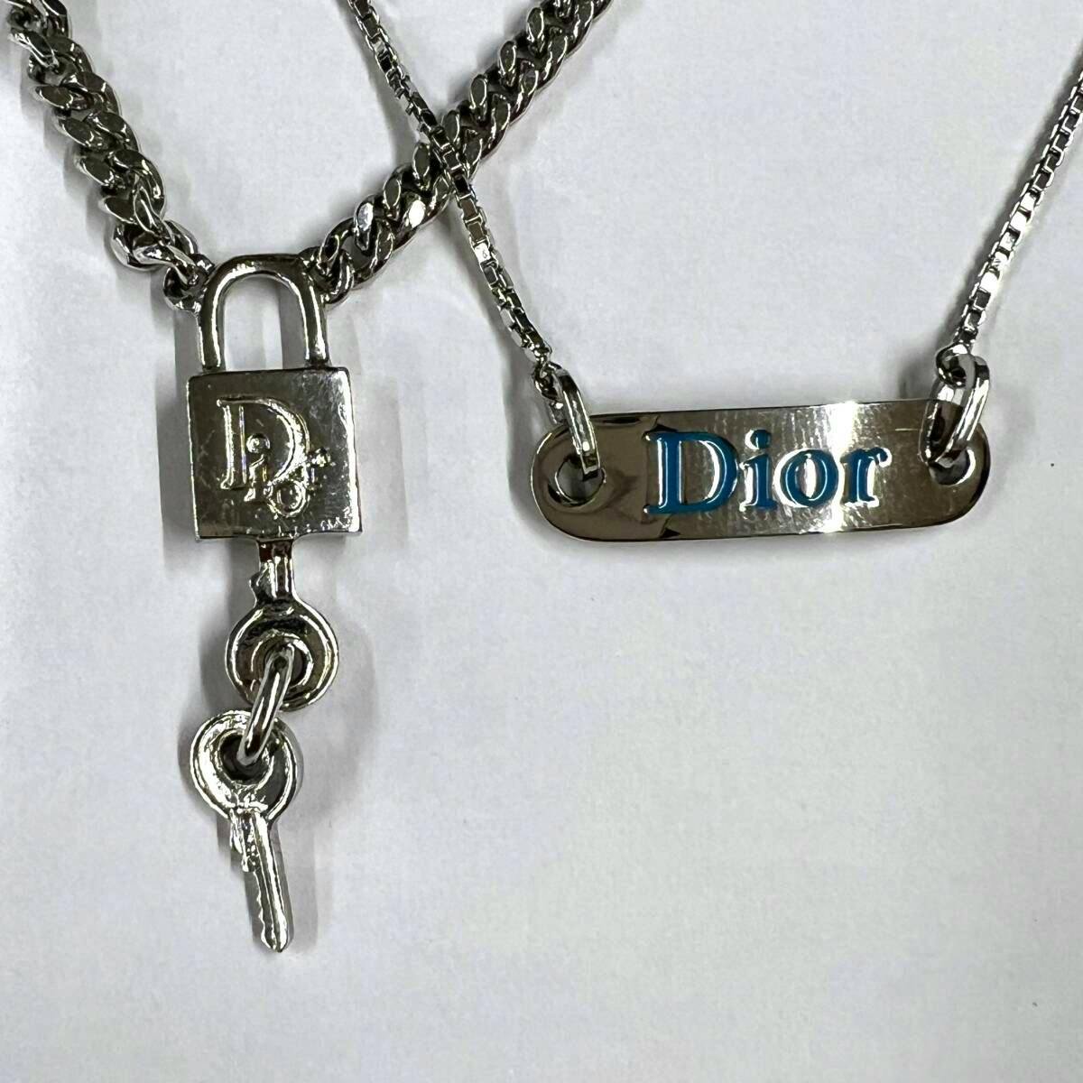Two silver Dior pendants on a white background: a padlock charm with a small key and a rectangular plate engraved "Dior".
