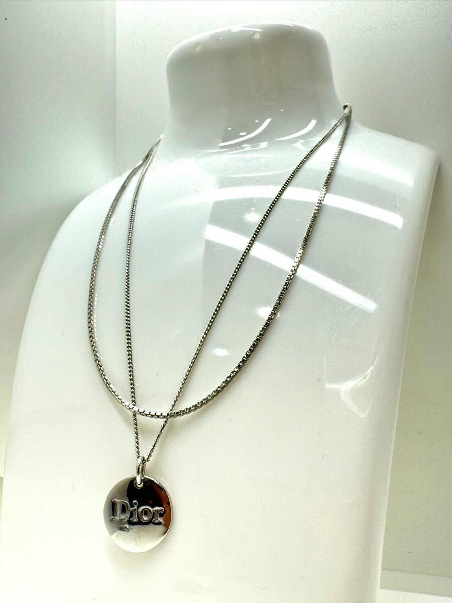 Silver Christian Dior necklace with a round pendant reading "Dior" displayed on a white mannequin bust.