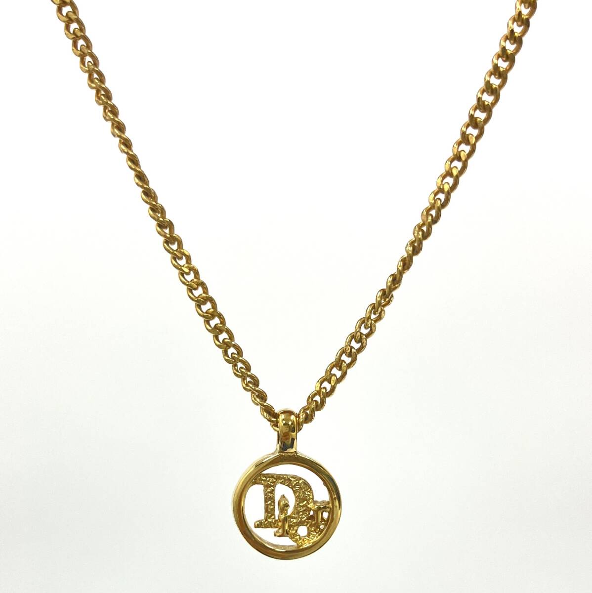 Gold-colored Christian Dior necklace with a circular Dior logo pendant and matching chain on a white background.
