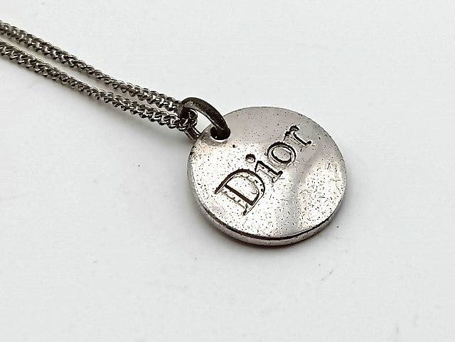 Close-up of a Christian Dior round logo plate necklace pendant stamped with "Dior" on a metal chain.