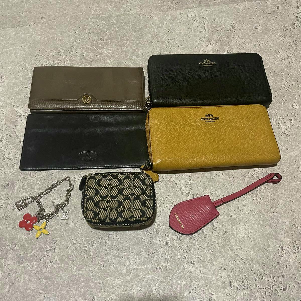 Several wallets and small accessories (including Coach wallets, a patterned coin pouch, a yellow zip-around wallet, a pink Coach tag, and a charm) arranged on a stone surface.