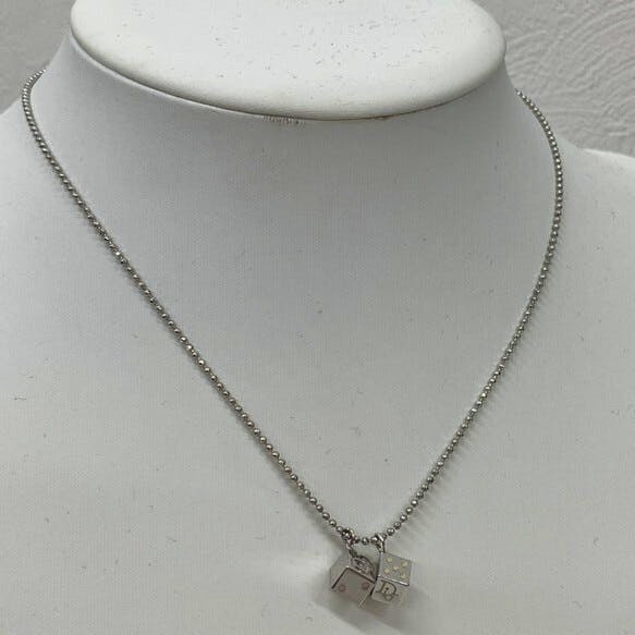 Metal ball-chain necklace with two cube (dice) Dior charms displayed on a white mannequin bust.