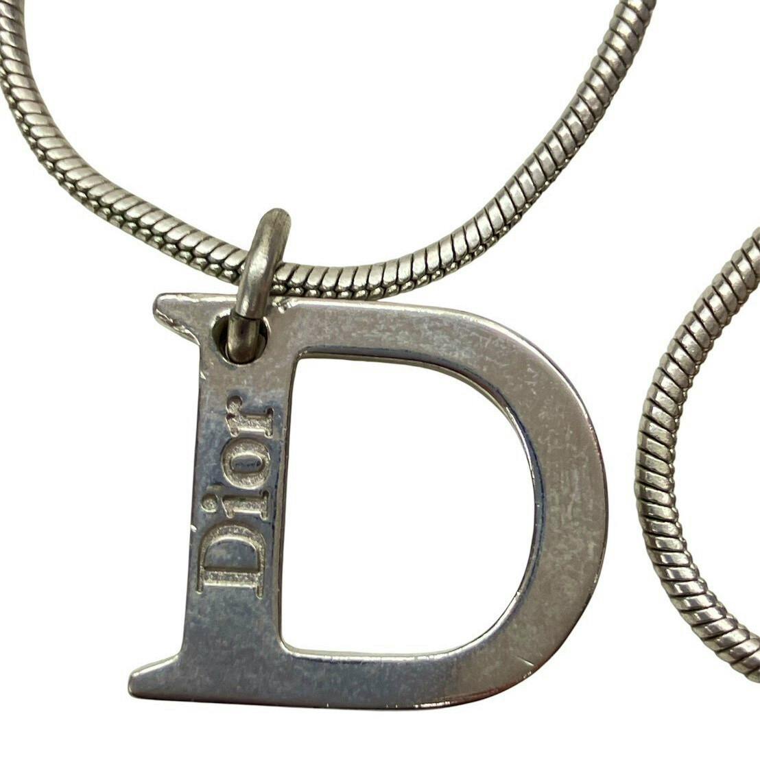 Close-up of the Christian Dior silver-color D-shaped pendant with "Dior" engraving hanging on a snake chain necklace.