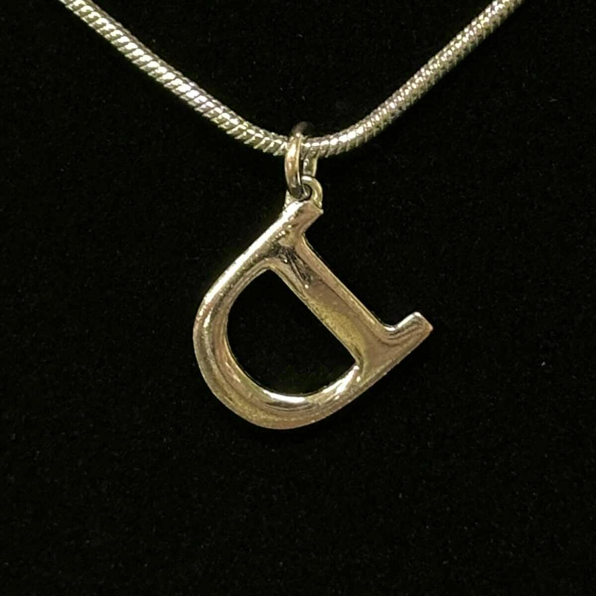 Silver D-shaped Christian Dior pendant on a snake chain against a black background.