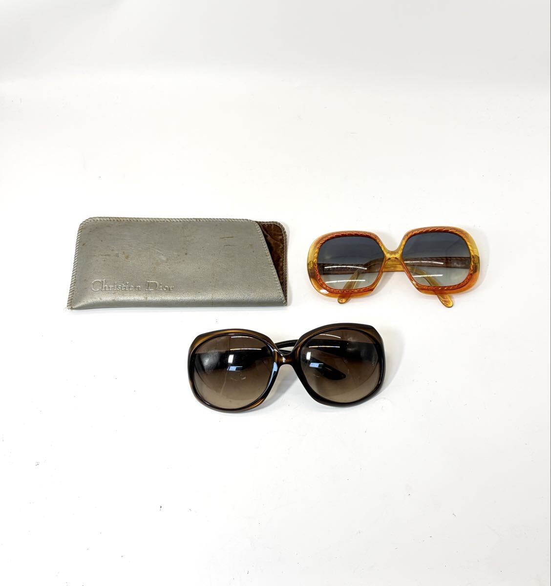 Two pairs of sunglasses and a silver Christian Dior case displayed on a white background.