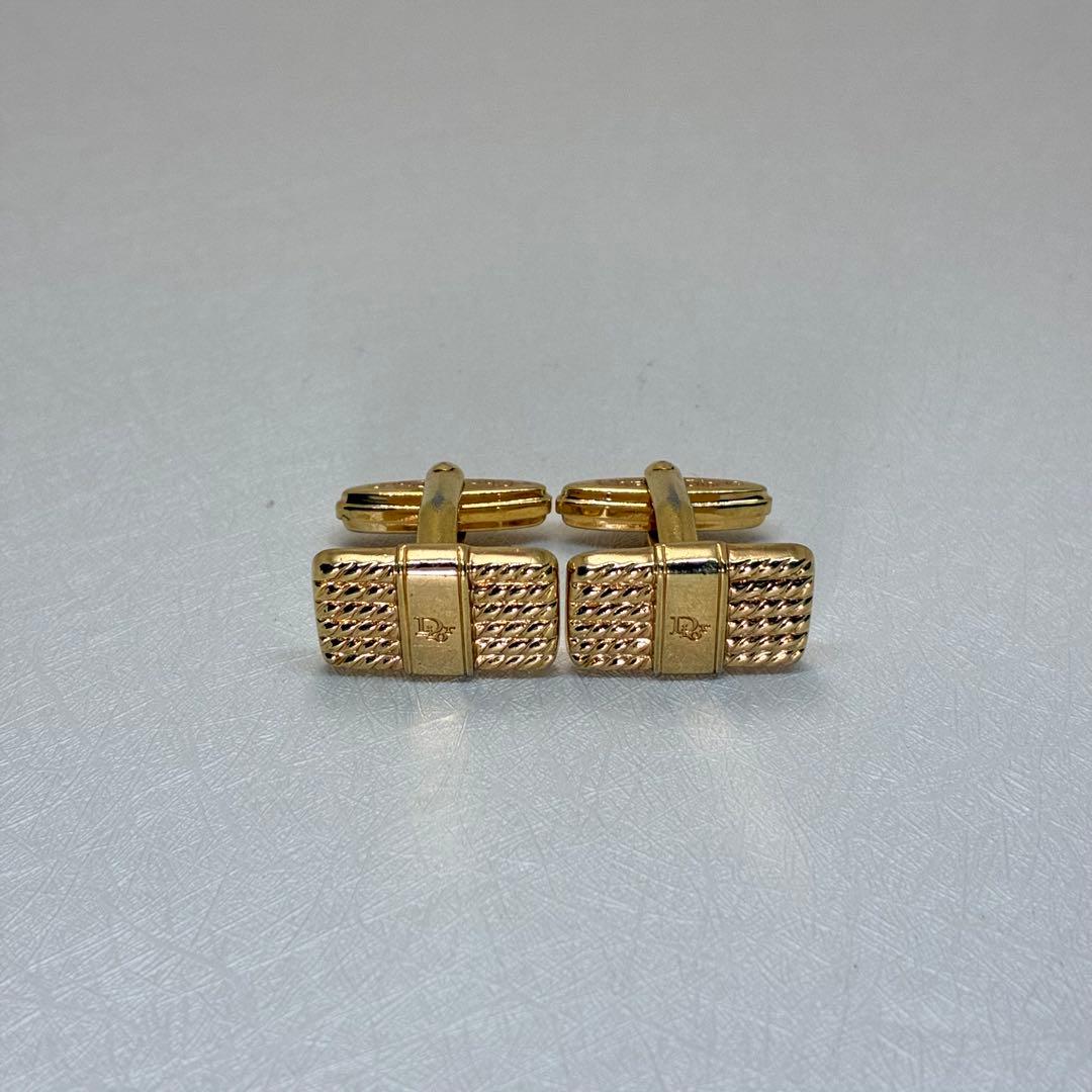 Pair of gold Christian Dior cufflinks on a light textured surface.