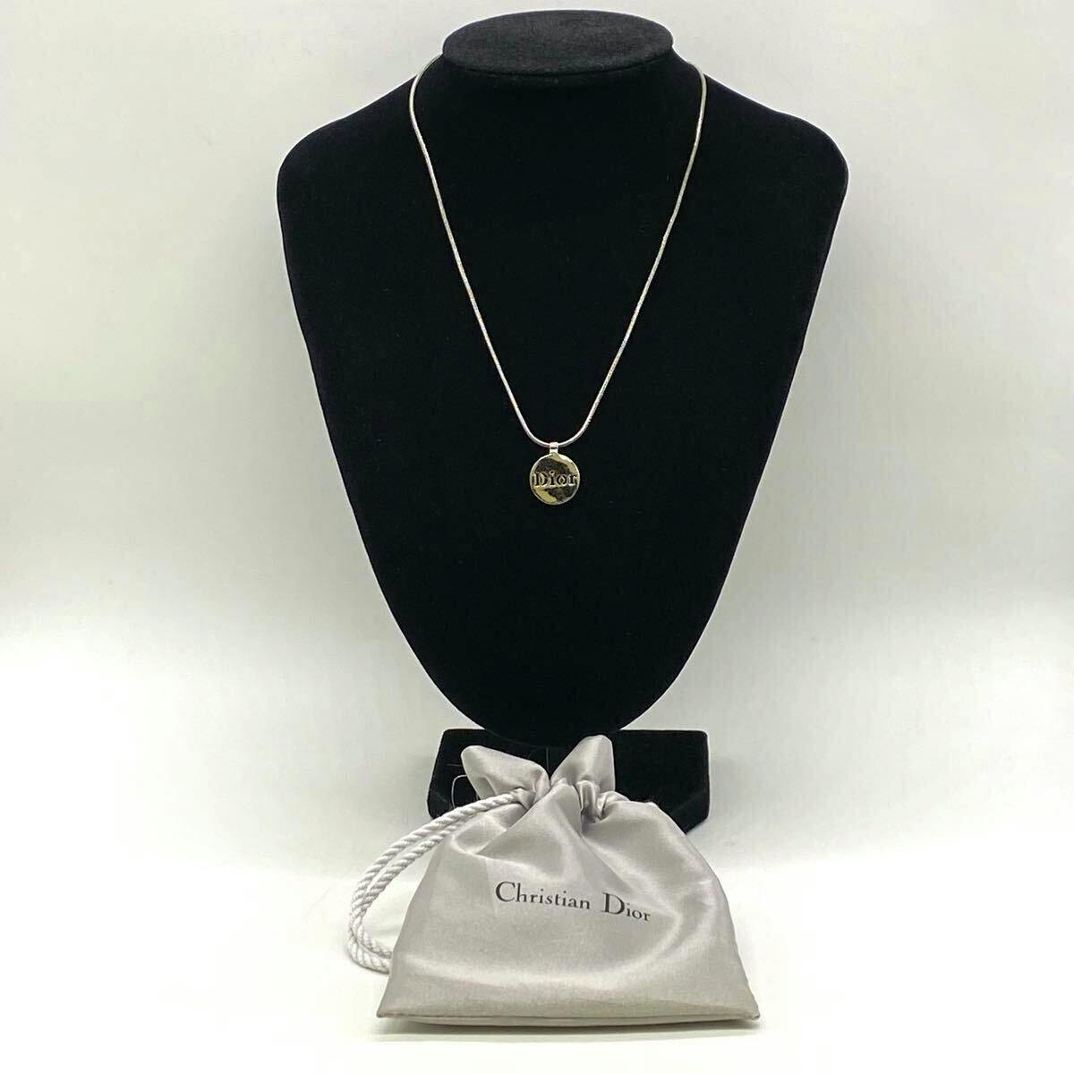 Silver-color Christian Dior necklace with a round Dior plate pendant displayed on a black jewelry bust with a Christian Dior drawstring pouch in front.