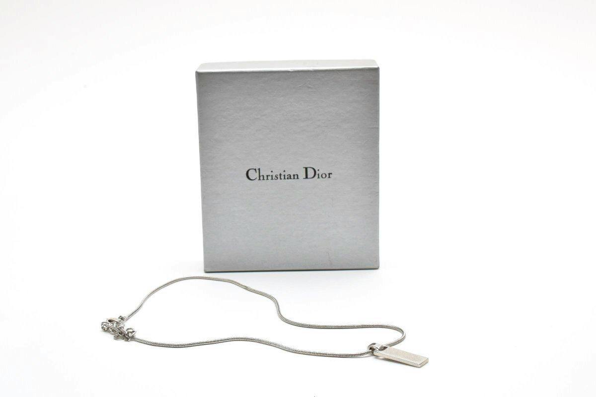 Silver Christian Dior necklace with a rectangular dog tag pendant displayed in front of a Christian Dior box on a white background.