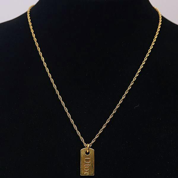 Gold-colored Christian Dior dog tag necklace displayed on a black jewelry bust.