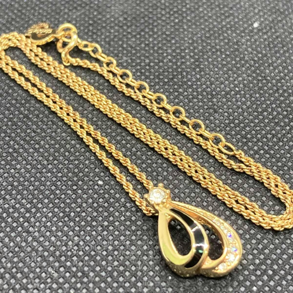 Gold-tone Christian Dior necklace with a teardrop pendant featuring black onyx inlay and rhinestone accents shown on a textured black surface.