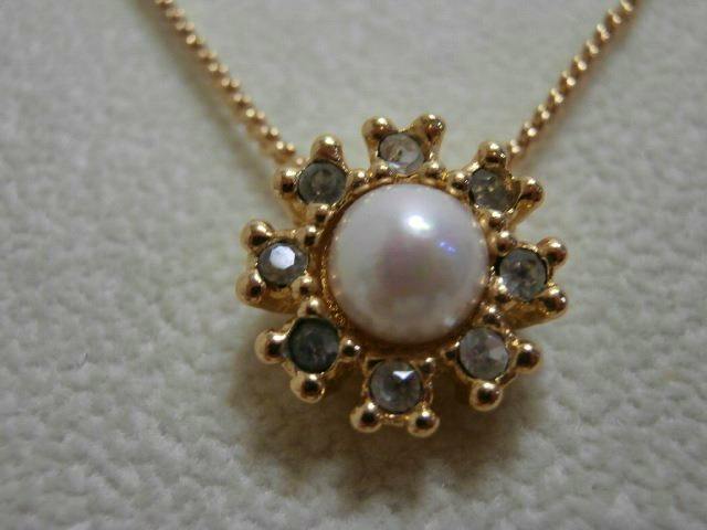 Close-up of the Christian Dior necklace's gold-tone flower-shaped pendant with a central faux pearl on a chain.