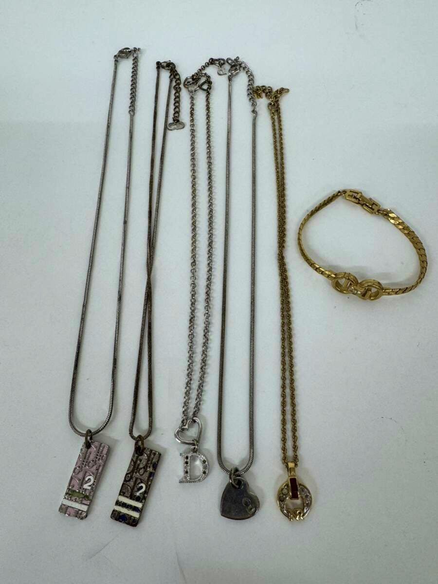Multiple metal necklaces with various pendants and a gold-tone bracelet arranged on a white background.