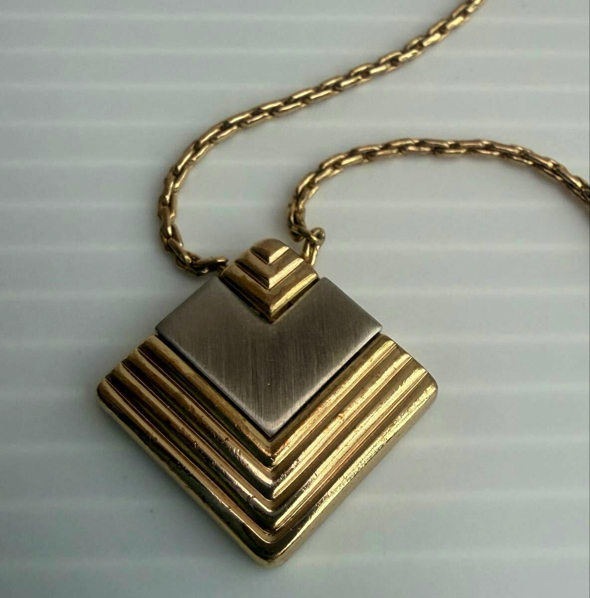 Close-up of the Christian Dior necklace showing a gold chain and a layered gold-and-silver geometric pendant on a light background.