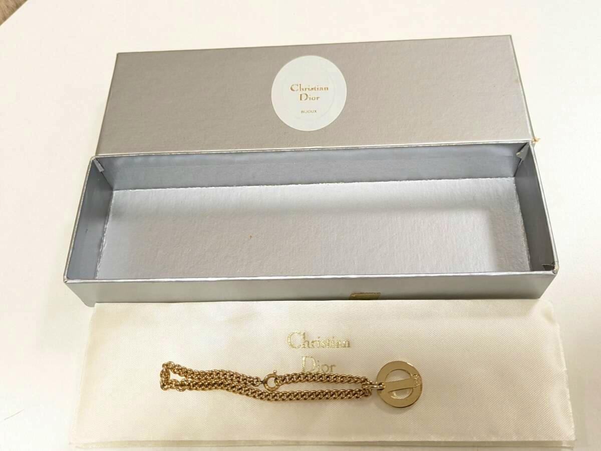 Gold-color Christian Dior bracelet with a round charm shown with its box and pouch.