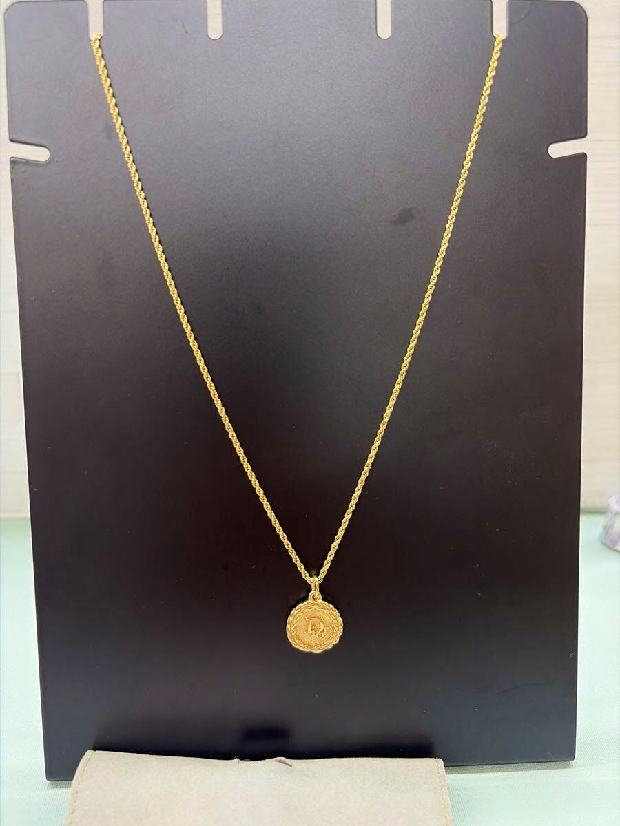 Gold-color Christian Dior circle-logo necklace with chain and pendant hanging on a black display board.