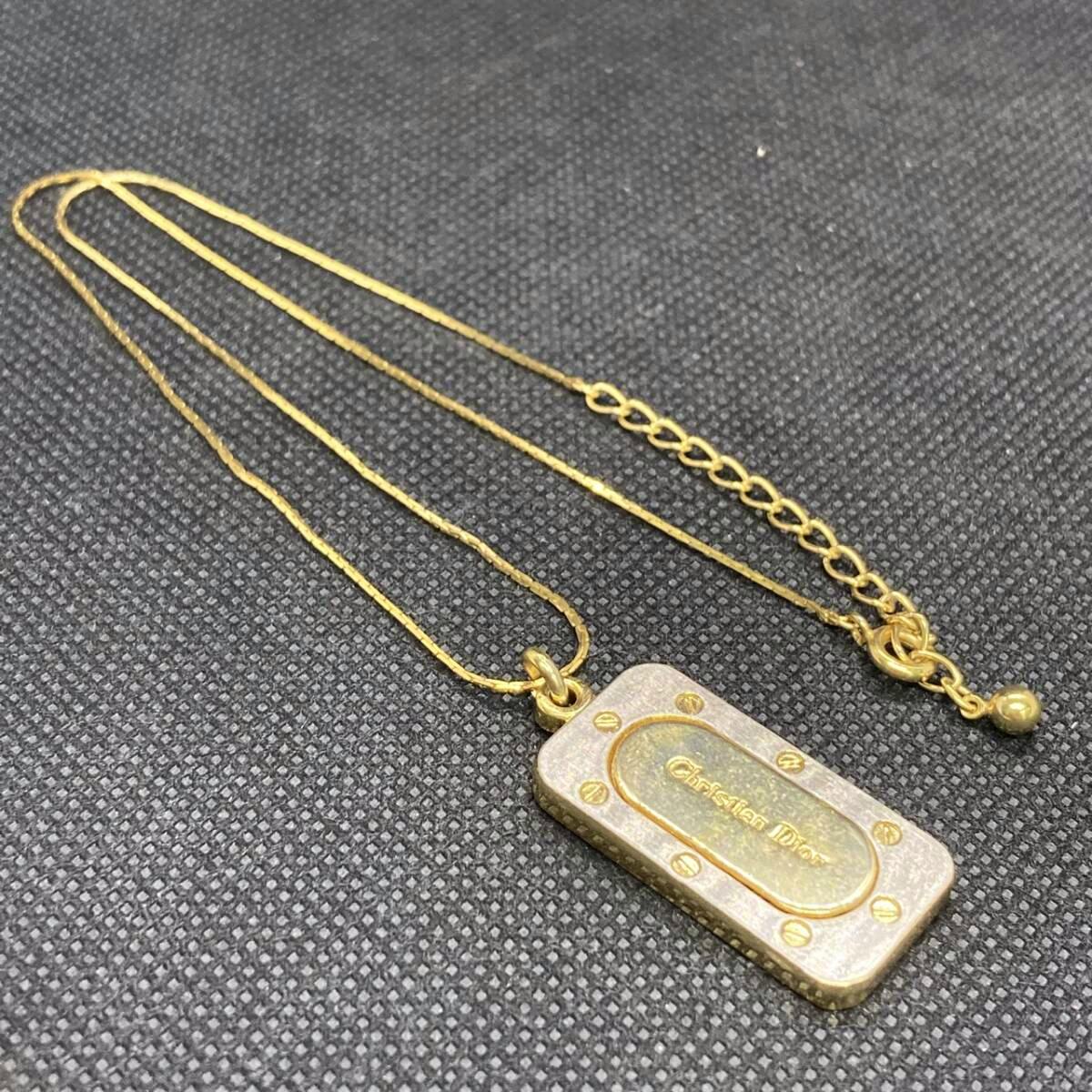 Gold-plated Christian Dior necklace with a rectangular logo pendant and adjustable chain on a dark textured background.