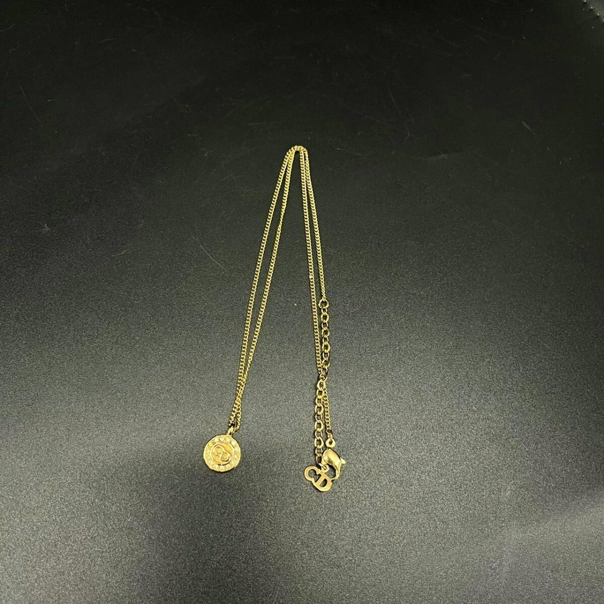 Gold-colored Christian Dior necklace with a round pendant, clasp, and extender chain laid on a dark background.