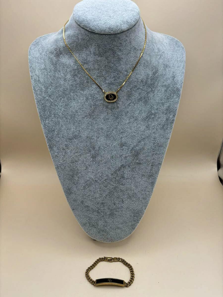 Gold-color Christian Dior necklace on a gray display bust with a gold bracelet placed below on a beige background.