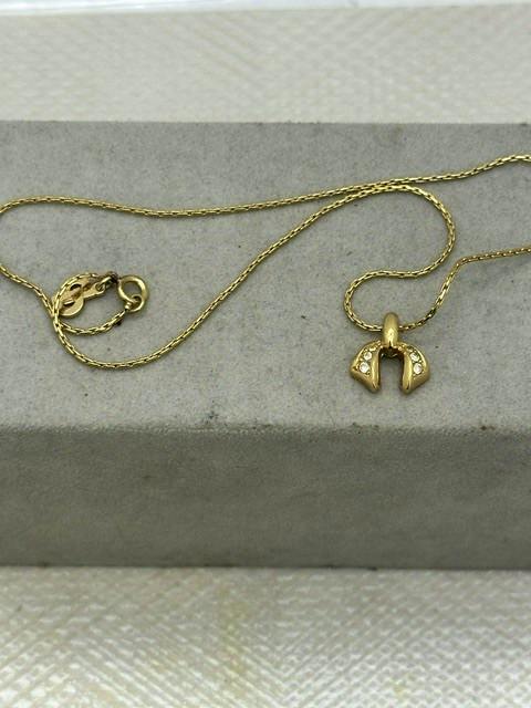 Gold-tone Christian Dior necklace with a small pendant and lobster clasp laid on a gray display surface.