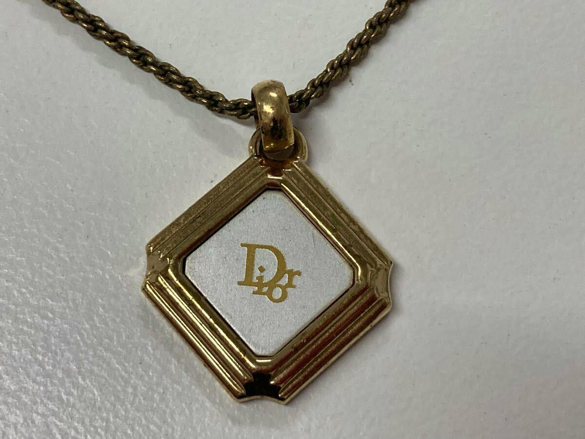 Close-up of a gold-colored Christian Dior necklace pendant on a rope-style chain showing a square decorative frame with the Dior logo.