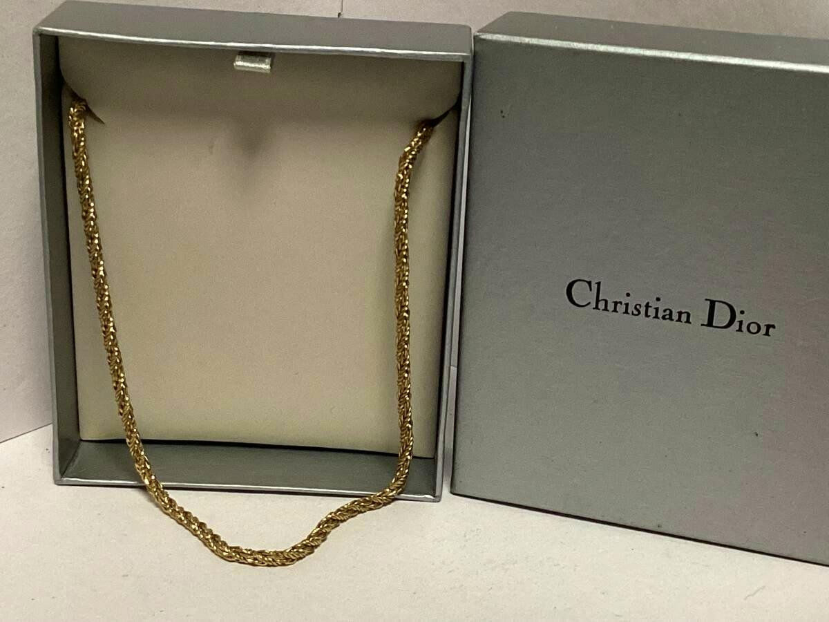Gold-colored necklace displayed inside an open Christian Dior jewelry box.