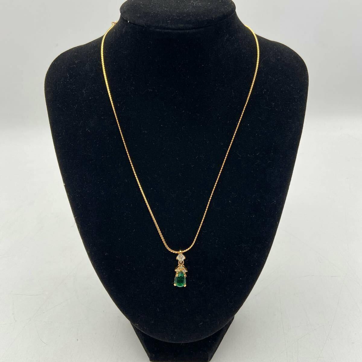 Gold-colored Christian Dior necklace with a green teardrop pendant displayed on a black jewelry bust.