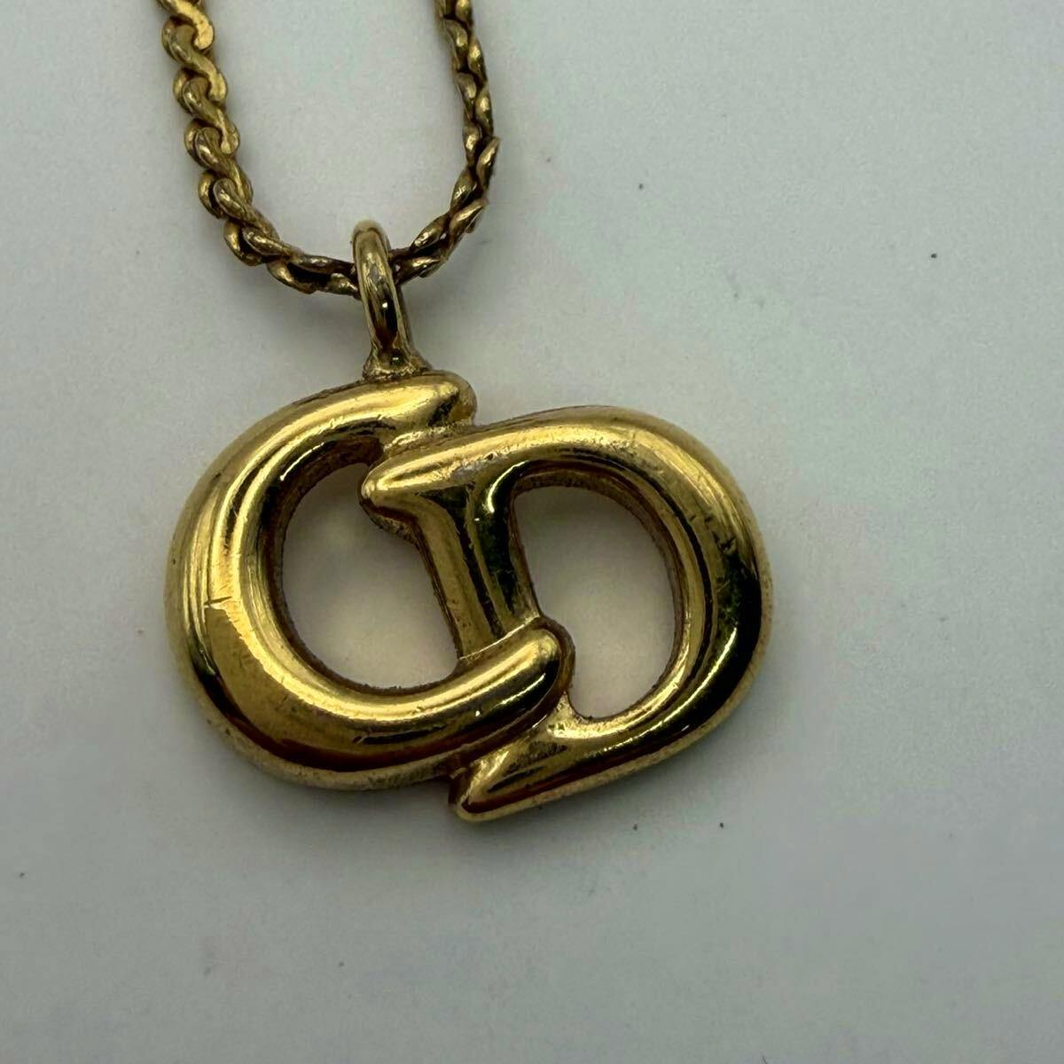 Close-up of the gold-color Christian Dior necklace pendant showing interlocking "CD" letters and part of the chain on a white background.