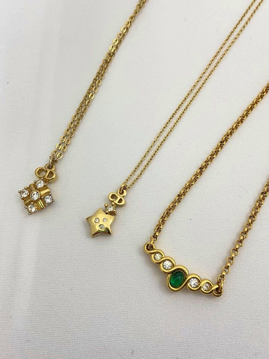 Three gold-colored Christian Dior necklaces with different pendants laid flat on a white background.