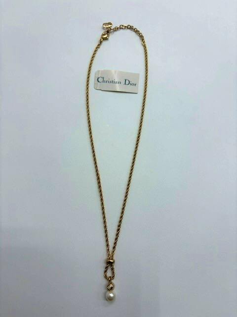 Gold-colored Christian Dior necklace laid flat on a white background with a hanging pearl pendant and a small Christian Dior tag.
