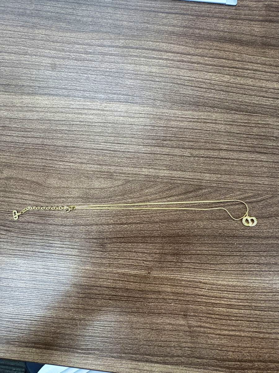 Gold-color Christian Dior necklace with chain and round pendant shown laid flat on a wood surface.