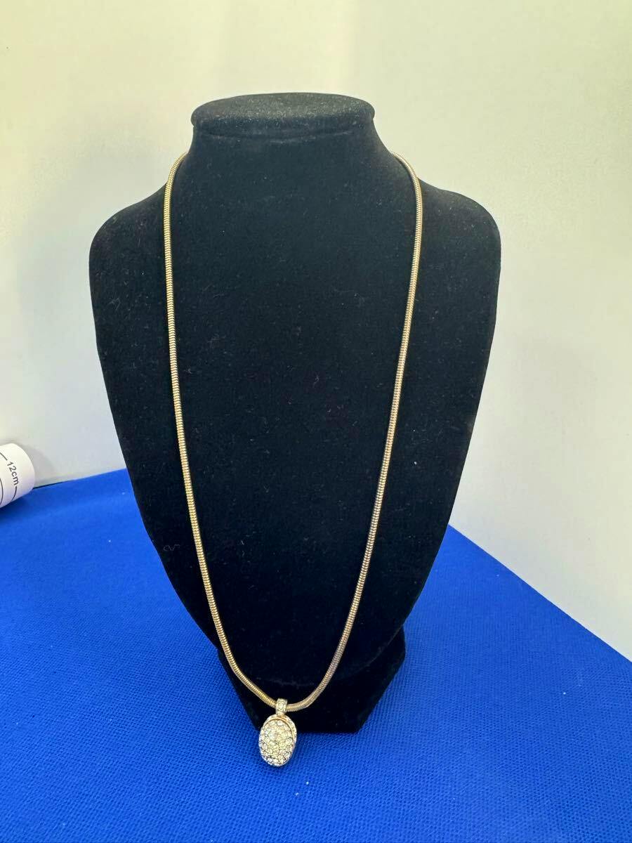 Gold-colored necklace with a rhinestone-studded oval pendant displayed on a black bust.