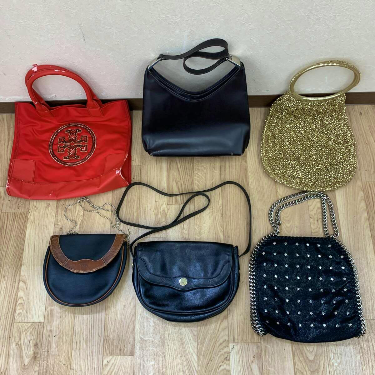 Six handbags of various styles and colors arranged on a wood floor, including a red tote, black shoulder bags, a gold beaded bag, and smaller chain-strap bags.