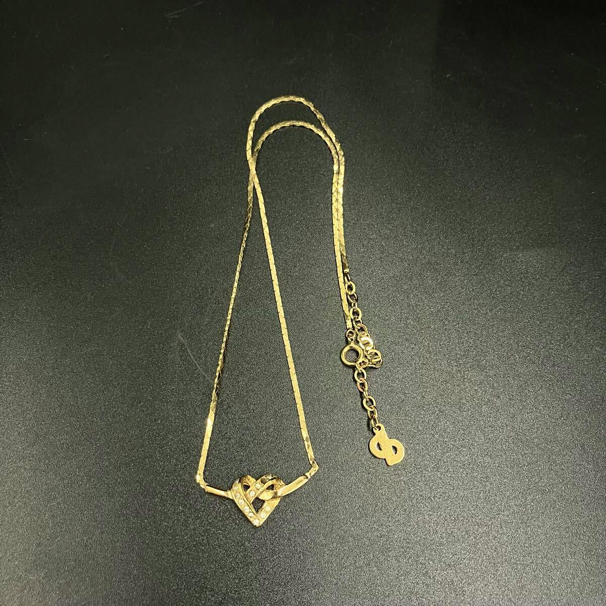 Gold-colored Christian Dior heart-motif necklace with rhinestone accents laid flat on a dark surface, showing the chain and clasp.