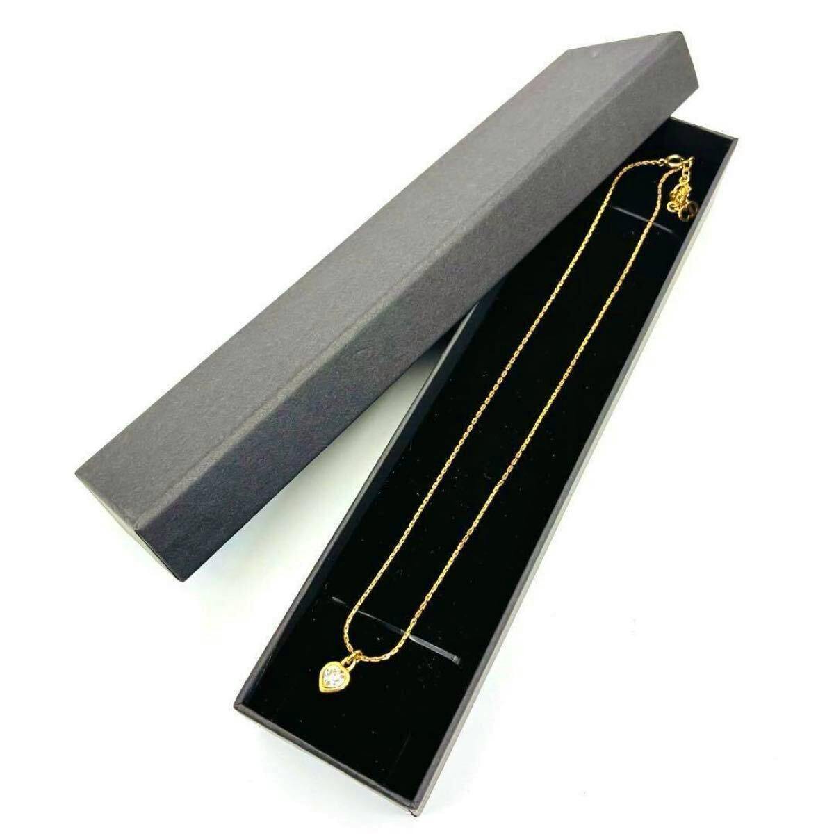 Gold-tone heart pendant necklace placed inside a long black jewelry box with the lid partially open.