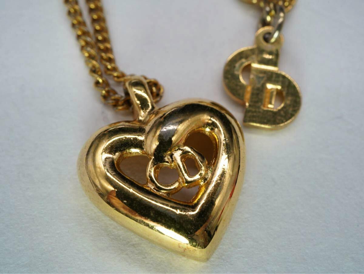 Close-up of a gold-tone Christian Dior heart pendant necklace with a small "CD" logo charm on a light background.