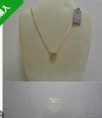 Gold-tone Christian Dior heart pendant necklace displayed on a jewelry bust with a Dior box visible at the bottom.