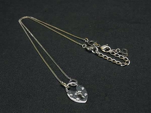 Silver-toned Christian Dior heart pendant necklace laid flat on black fabric showing pendant and chain.