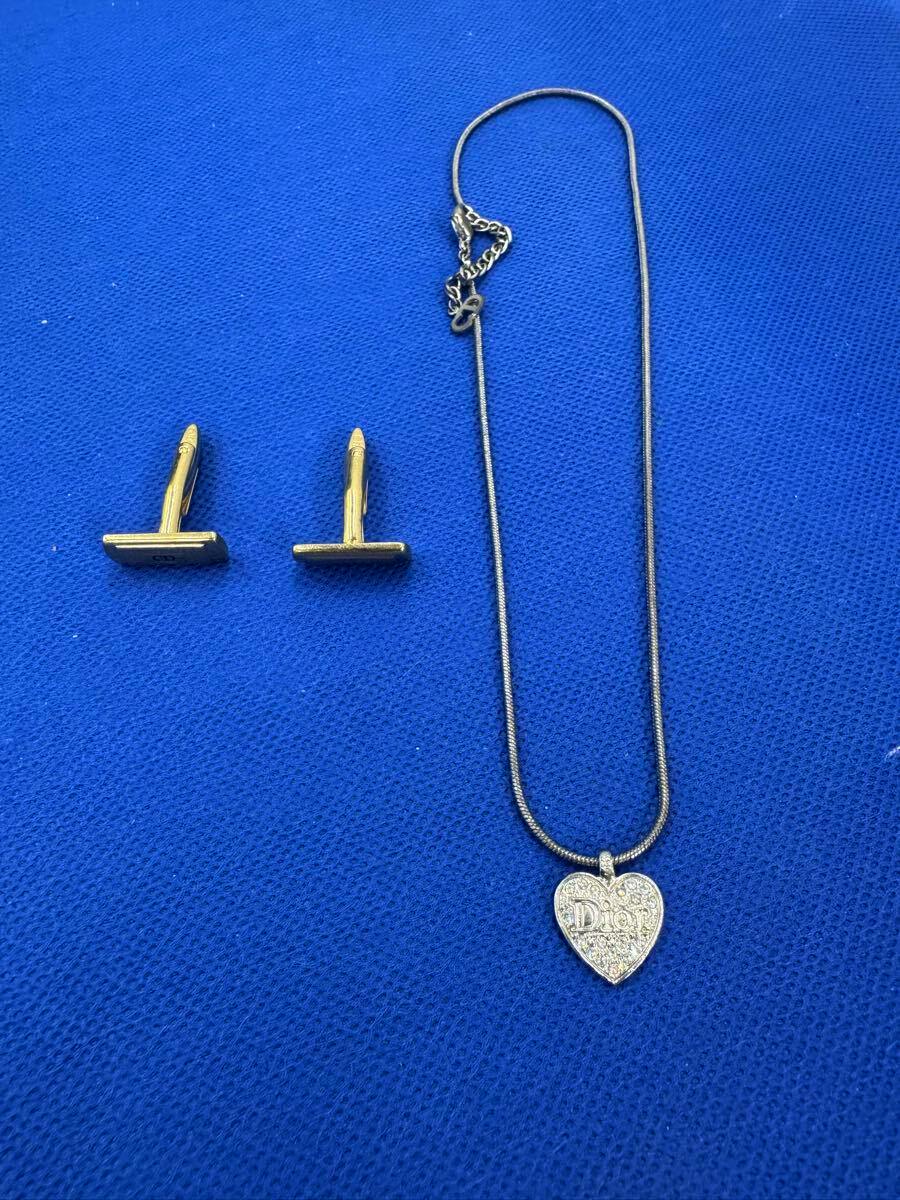 A Christian Dior heart rhinestone necklace with chain and a pair of T-shaped gold-tone earrings laid on blue fabric.