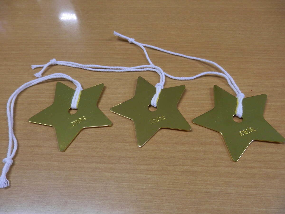 Three gold star-shaped Dior logo bag charms with white cords laid on a wooden surface.