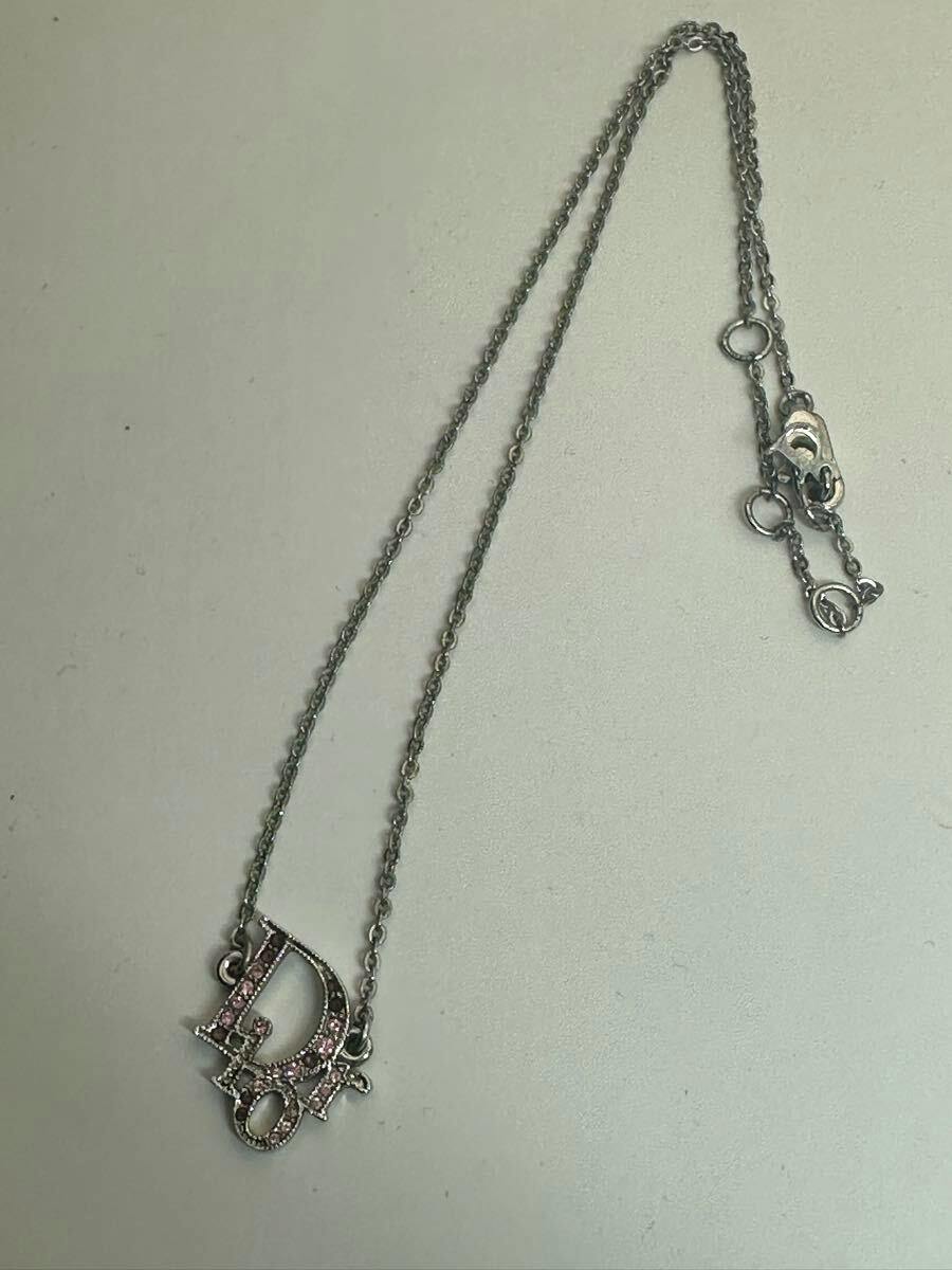 Silver-tone Christian Dior necklace with pink rhinestone "Dior" logo charm laid on a light background.