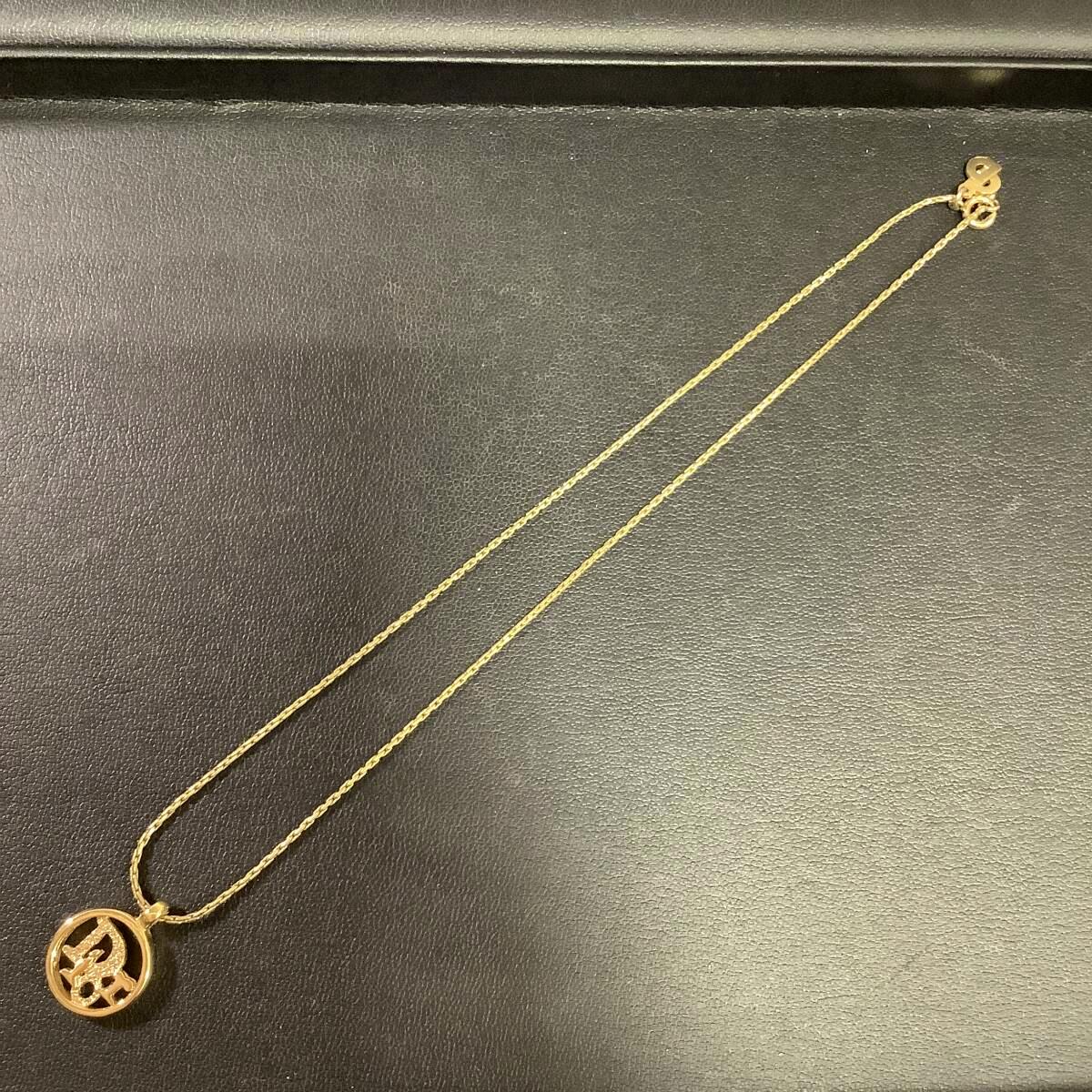 Gold-colored Christian Dior logo circle necklace laid flat on a black surface, showing the chain and pendant.