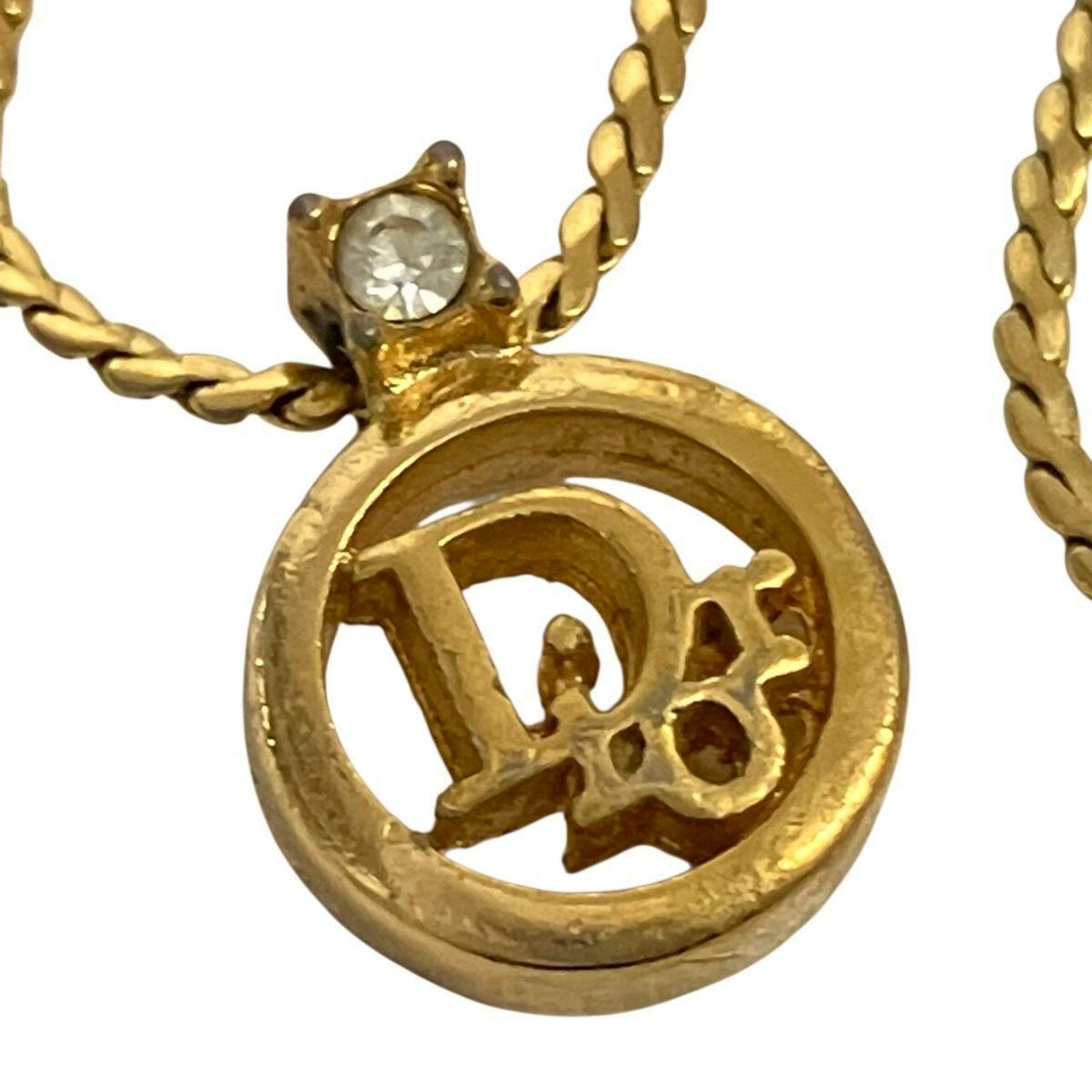 Close-up of the gold-colored Dior circle logo pendant with a small stone on its chain.