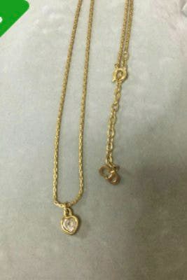 Gold-colored heart pendant necklace with a chain and extender clasp laid on a light surface.