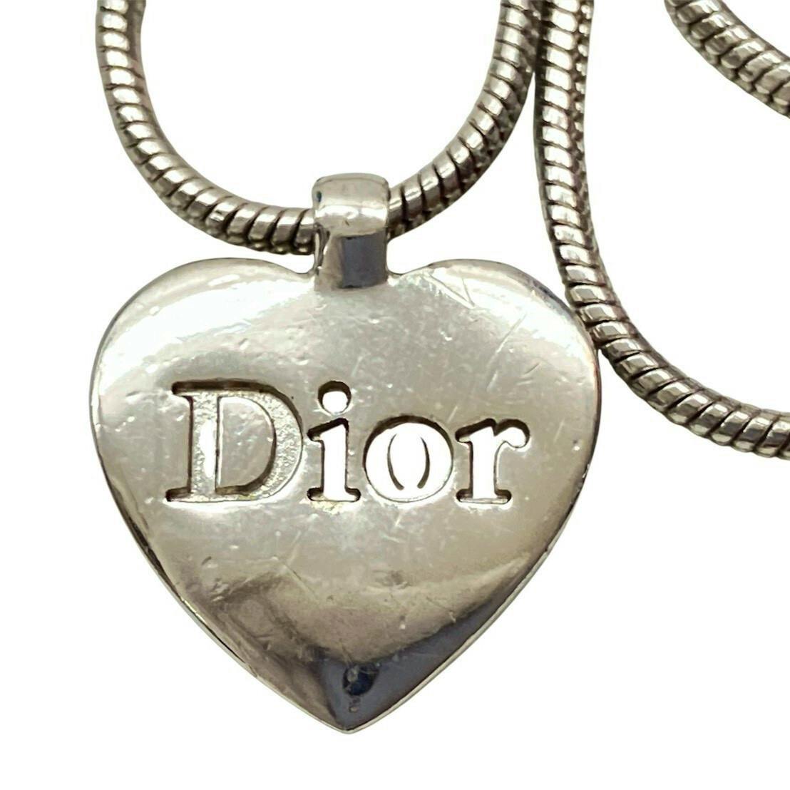 Close-up of a silver-colored heart-shaped Dior pendant necklace with the 'Dior' logo cut out and a snake-style chain.