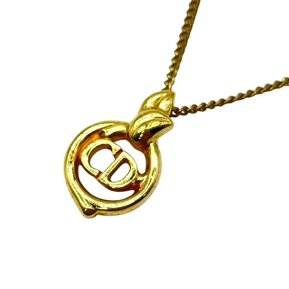 Gold-colored Christian Dior necklace pendant with a circular CD logo on a chain against a white background.