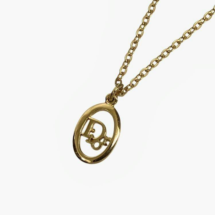 Gold-tone Christian Dior oval logo pendant on a chain photographed on a white background.