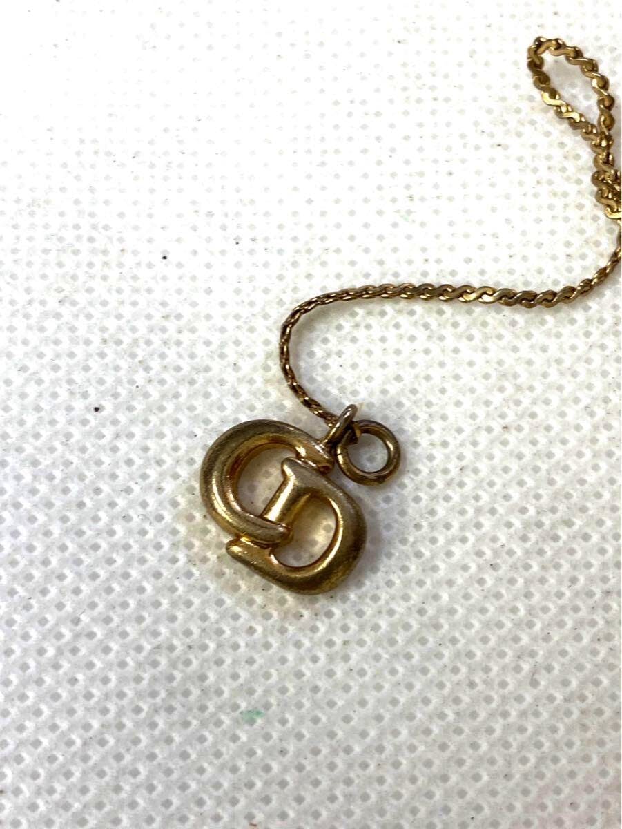 Gold-tone Christian Dior logo pendant necklace on a white textured background.
