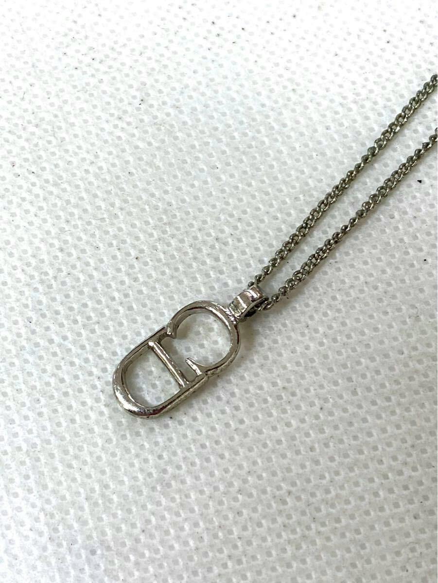 Close-up of a silver Christian Dior logo necklace pendant on its chain against a white textured background.